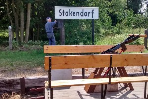 Das Bahnhofsschild in Stakendorf wird montiert.